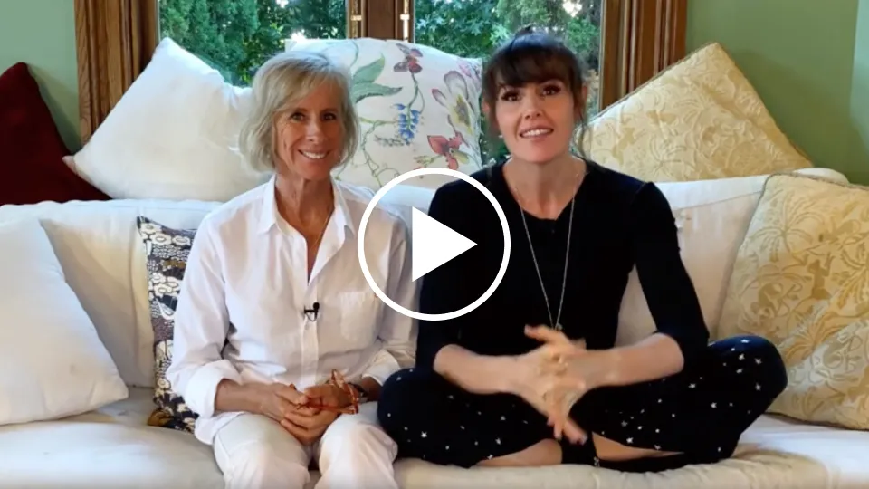 Two women on a couch with lots of cushions.