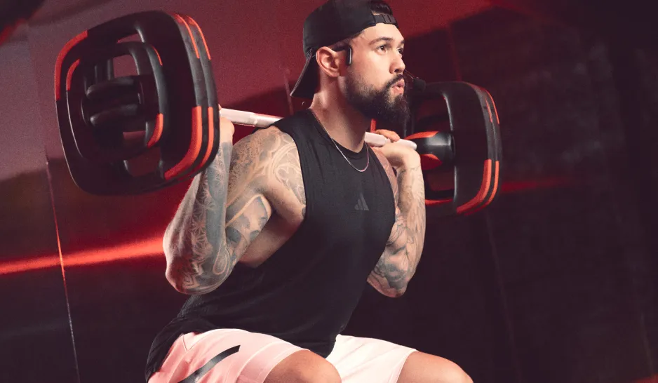 Male with tattoos on arms squatting with barbell on back