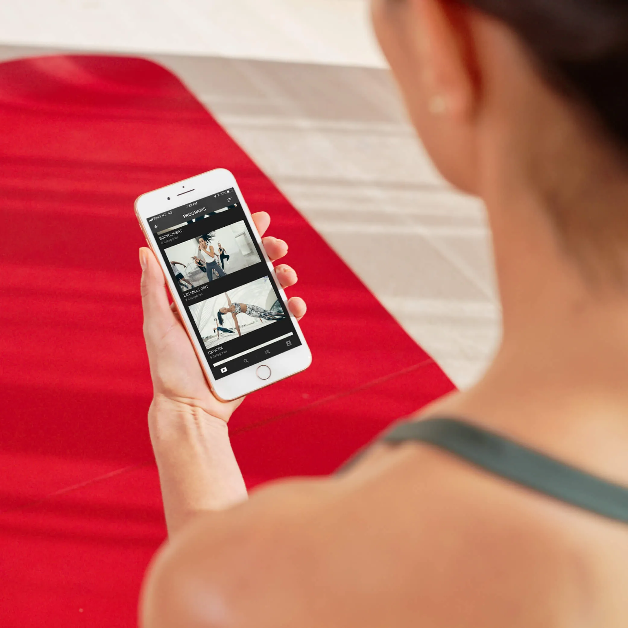 Over-the-shoulder view of a woman holding a smartphone displaying a fitness app with workout programs.