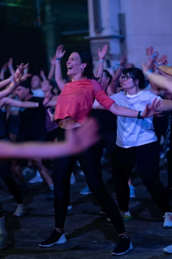 A woman in an orange top smiles as she takes part in a group workout with others