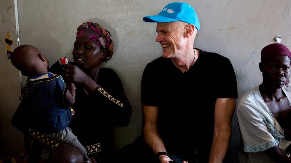 Phillip Mills in a blue hat with mother and child in Sudan