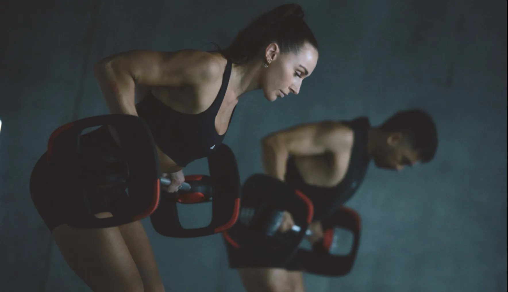 A woman and a man performing bent-over rows with barbells in a gym.