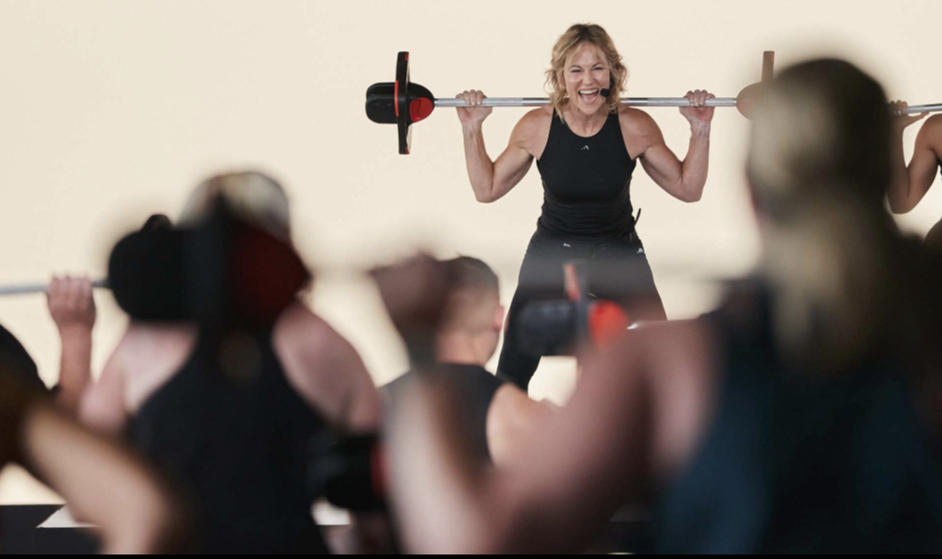 Les Mills Instructor leads busy group fitness class with barbell