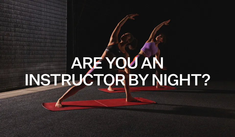 Two women performing side stretches on red yoga mats in a dimly lit gym with the text 'ARE YOU AN INSTRUCTOR BY NIGHT?' overlaid.