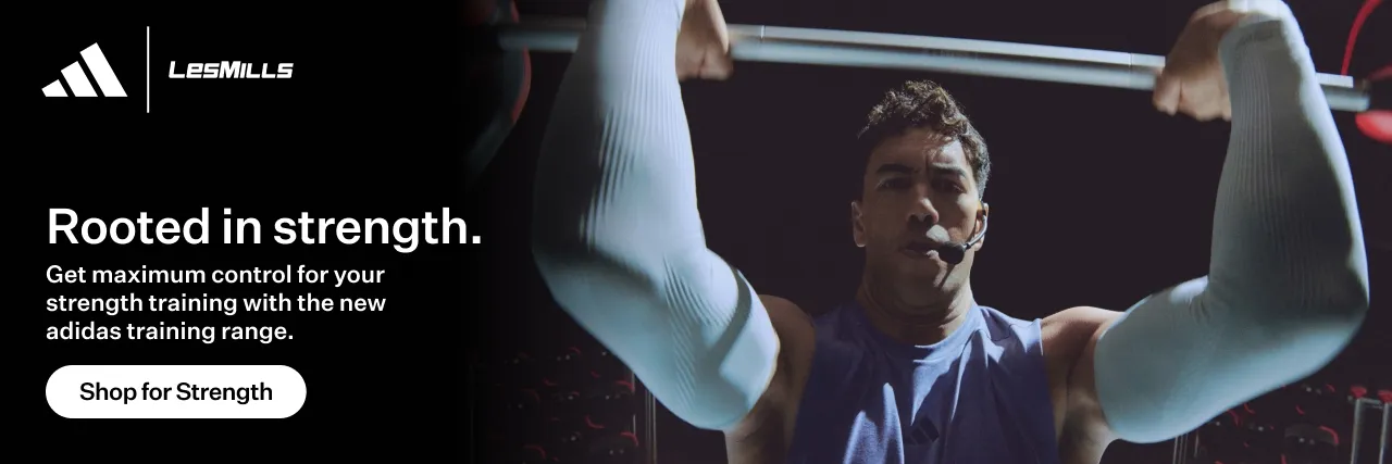 Man lifting a barbell overhead wearing white arm sleeves and a headset microphone in a gym setting.