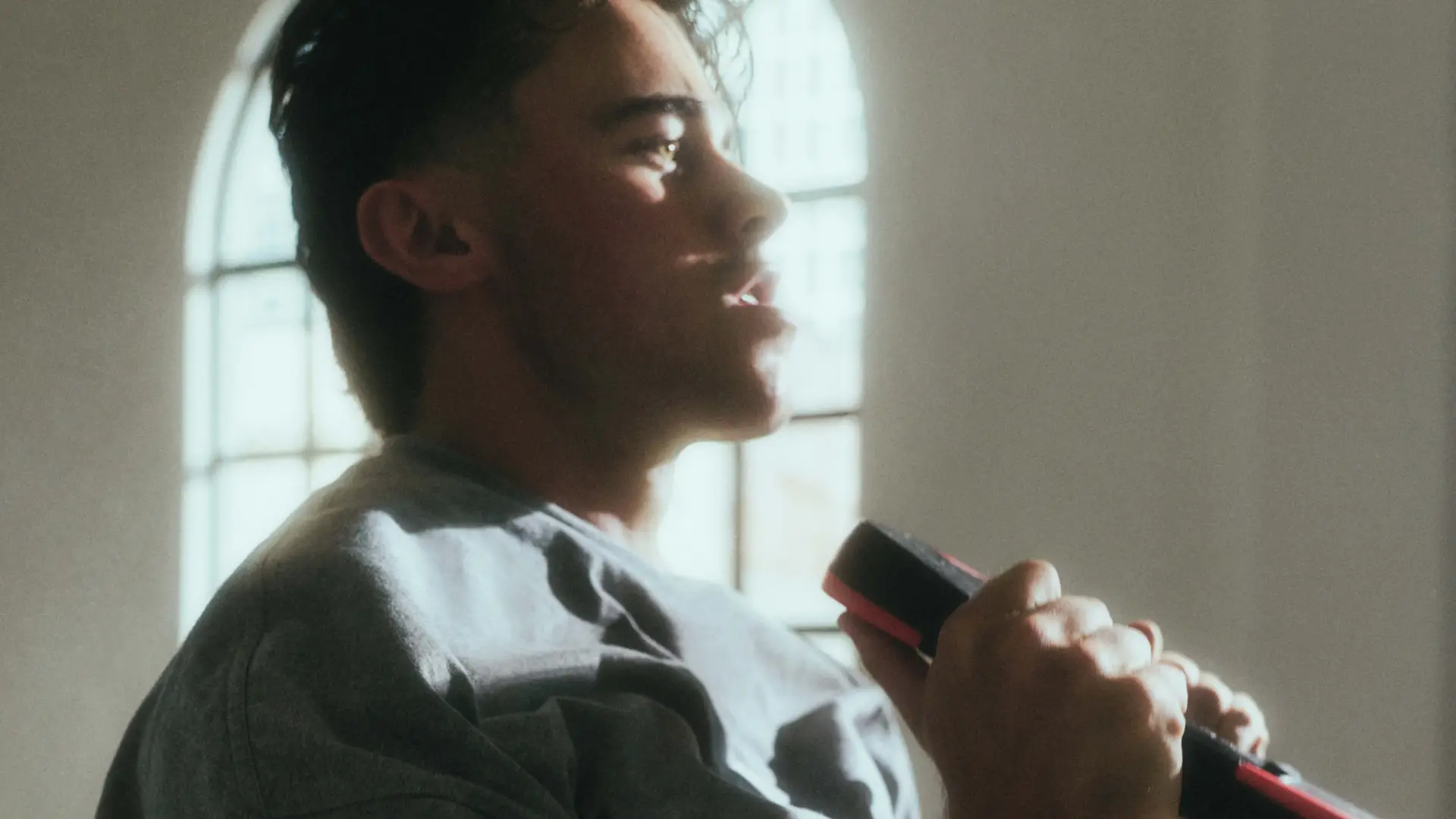 Side view of a man holding a dumbbell near a window with sunlight on his face.