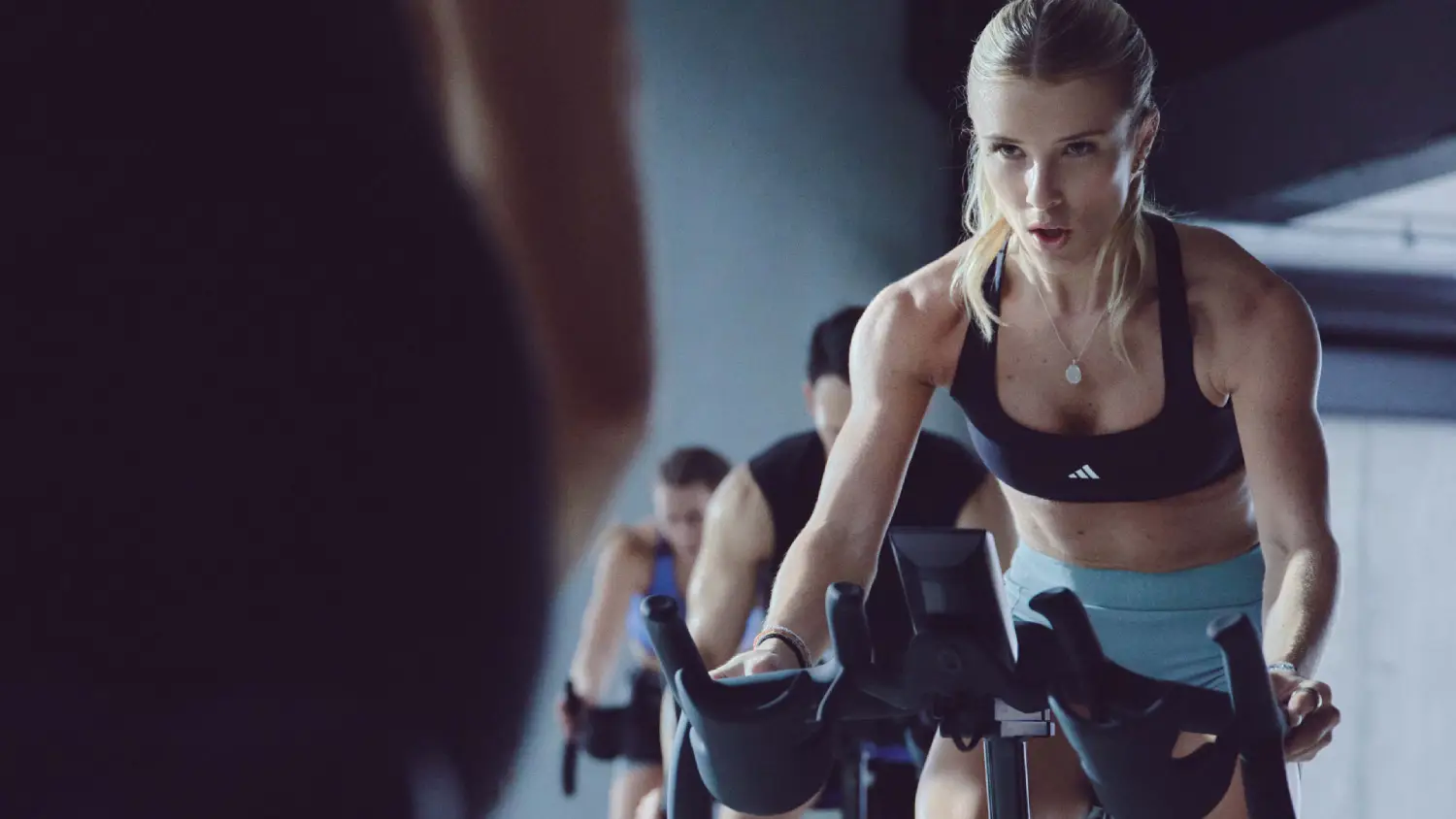 Athletic woman focused on indoor cycling class, with others biking behind her.