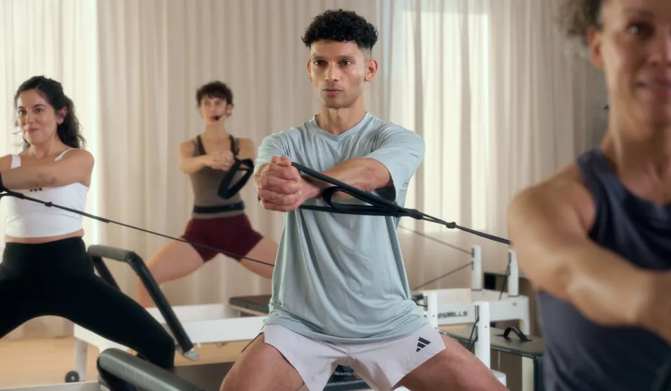 Group of people doing Pilates reformer exercises with resistance bands in a bright studio.