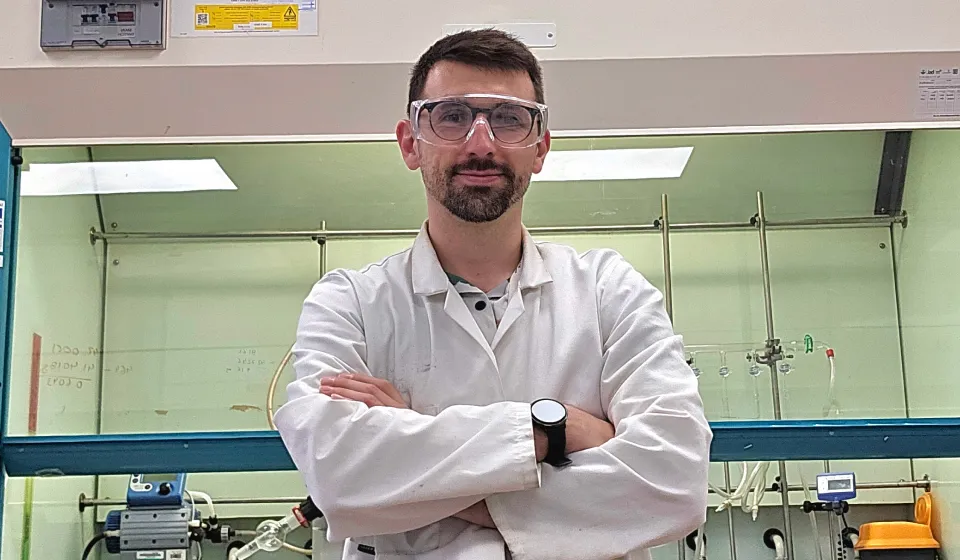 A man in a science lab in a white lab coat and protective glasses