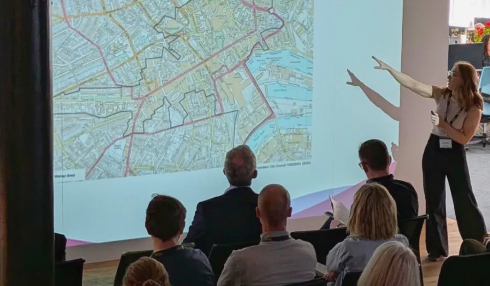 A standing woman presents a town planning map to a seated group
