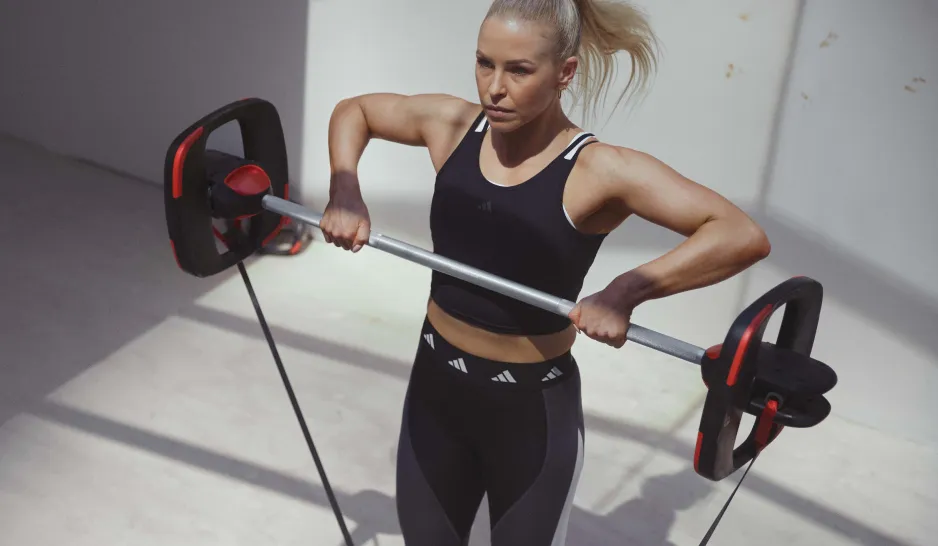 A blonde woman in black workout gear lifting a barbell with a resistance band