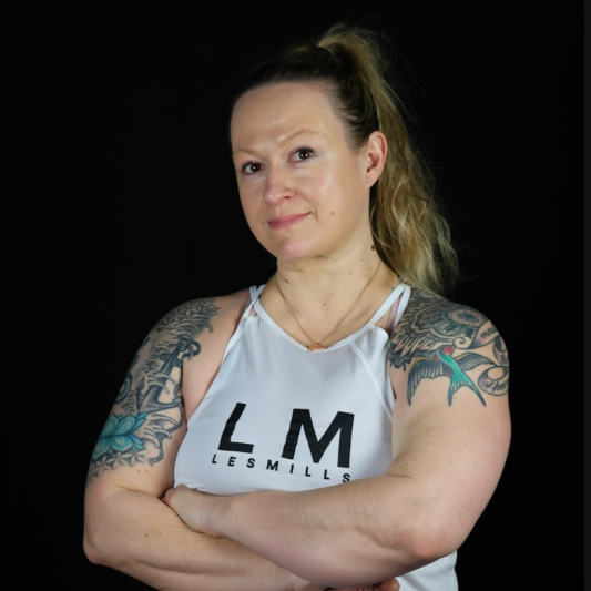 A woman with tattoos and a ponytail in a white Les Mills top