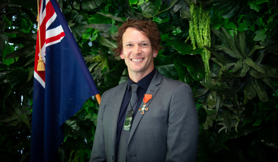 A man in a suit, with New Zealand flag and pounamu