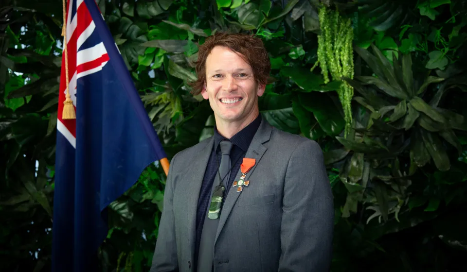 A man in a suit, with New Zealand flag and pounamu