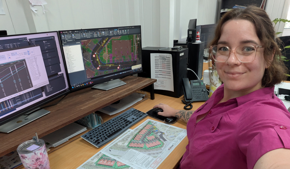 A woman with glasses in a pink shirt working at dual computer screens