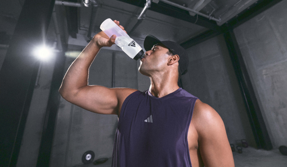 Man in a purple tank top drinking from an adidas drink bottle
