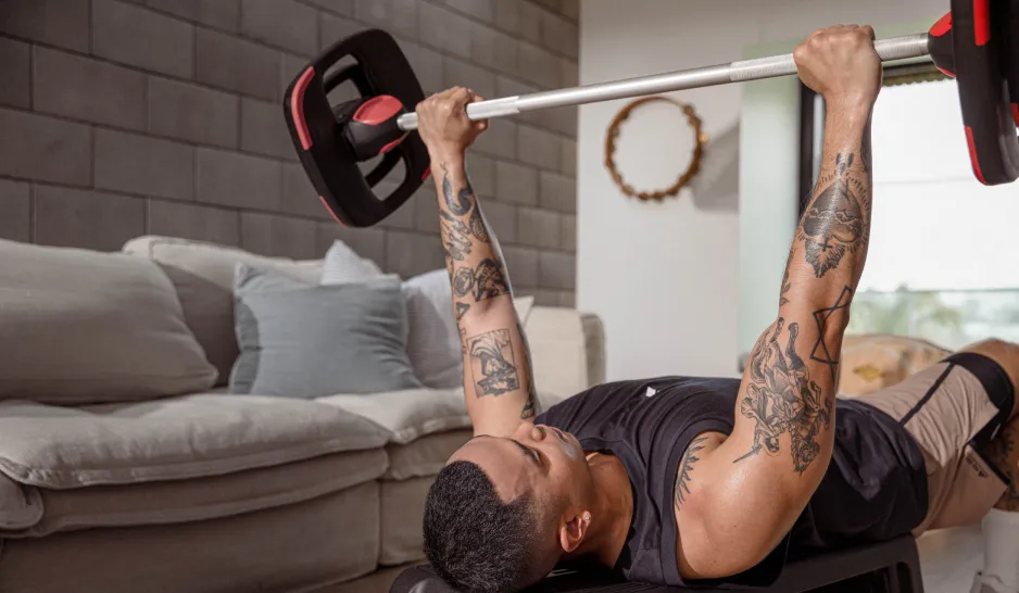 A man with tattoos does a bench press at home in a lounge