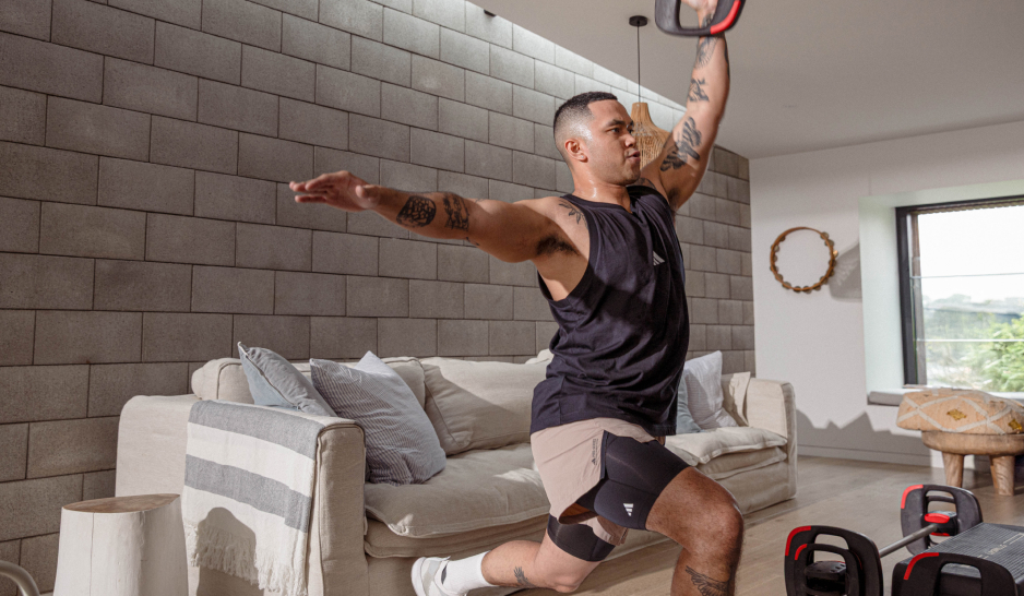 A man with tattoos lunges with a weight plate in front of a lounge suite