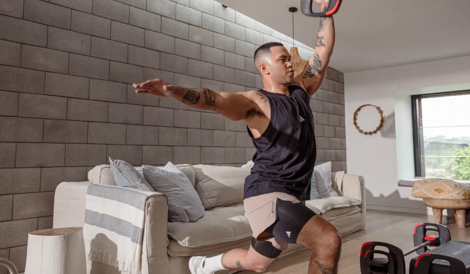 A man with tattoos lunges with a weight plate in front of a lounge suite