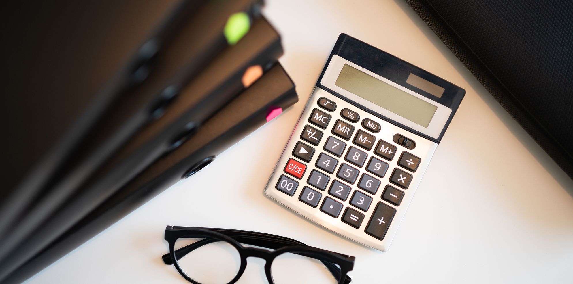 Calculator, reading glasses and black ring binders on a white office desk