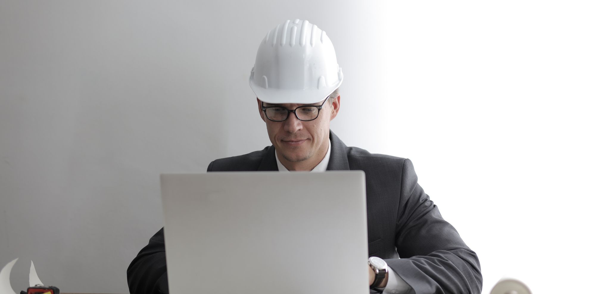 Engineer in a white hard hat and suit working on a laptop at an office desk