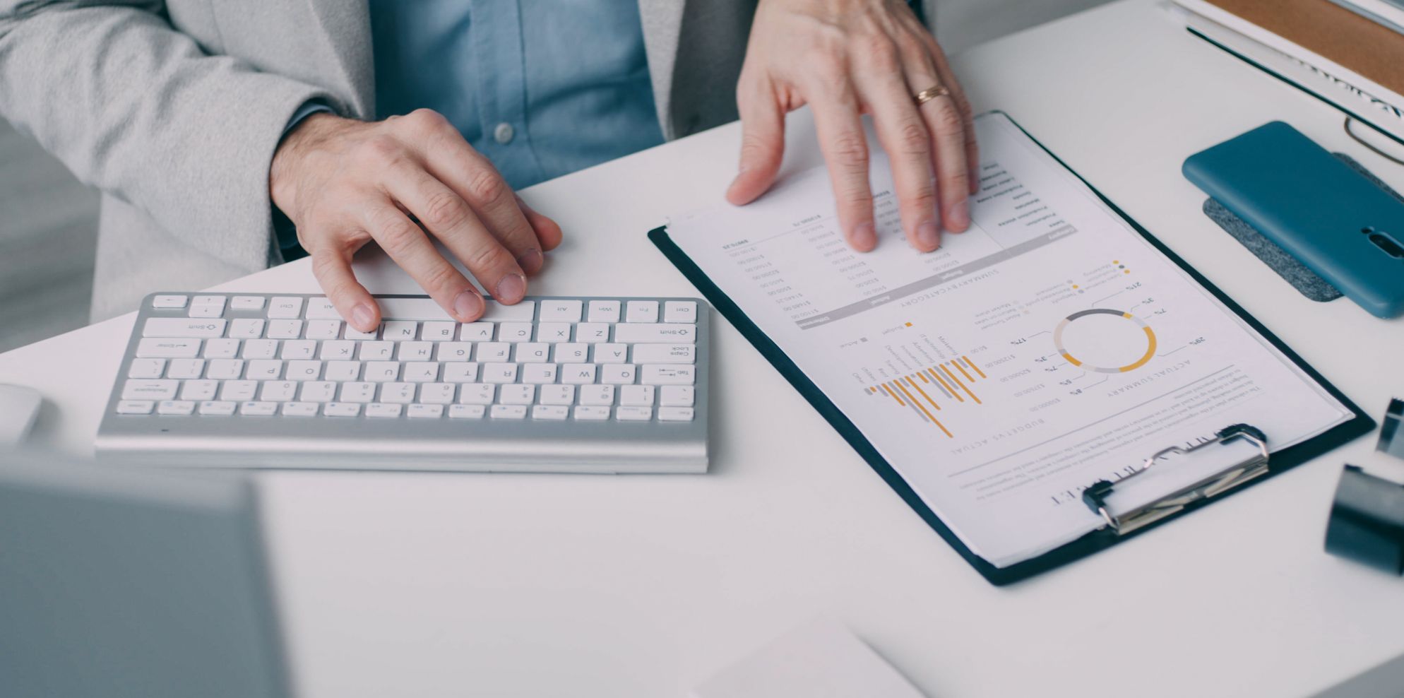 Hands reviewing a printed financial report with charts on a clipboard next to a keyboard