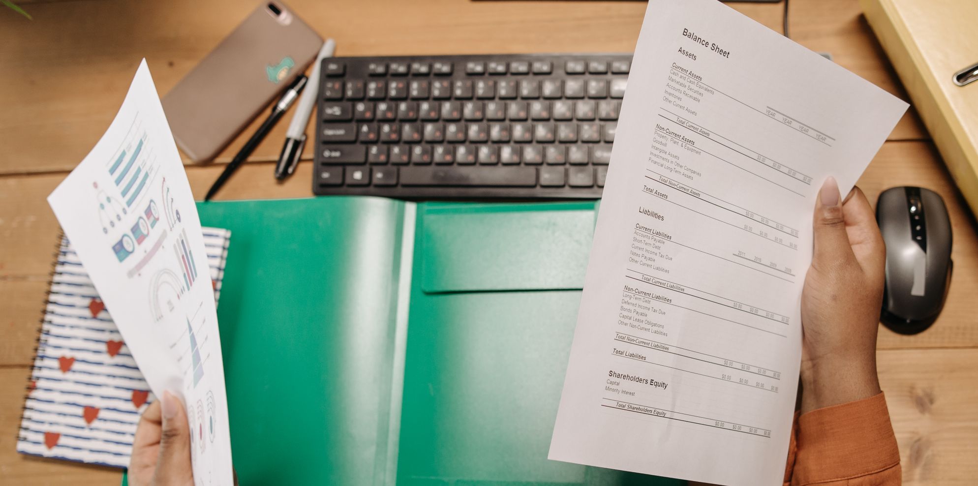 Hands holding a printed balance sheet showing current assets and liabilities above a desk with a keyboard