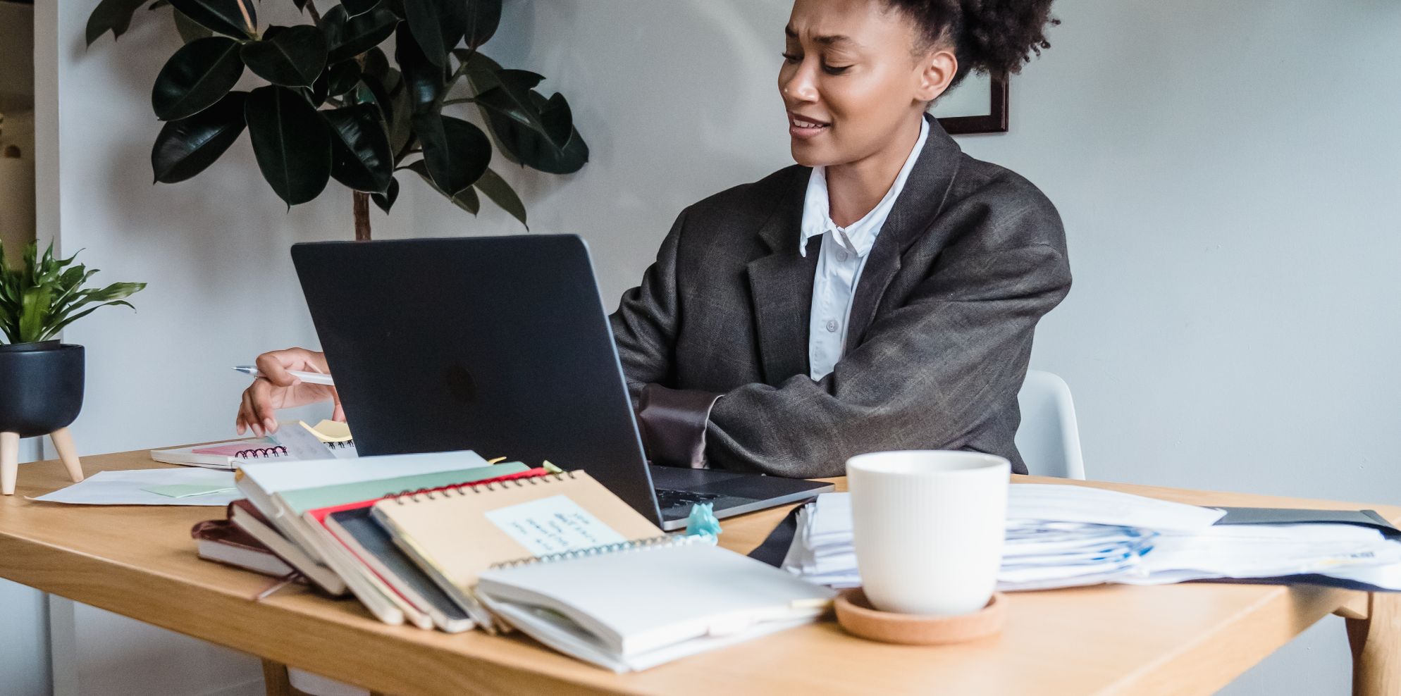Finance professional on a laptop call at a desk with notebooks, paperwork and a coffee cup