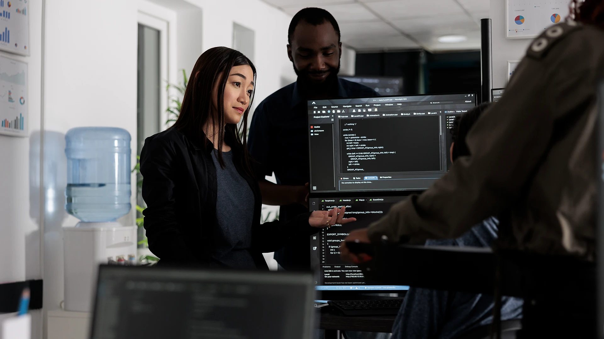 Two coworkers discussing code displayed on a computer monitor in an office setting.