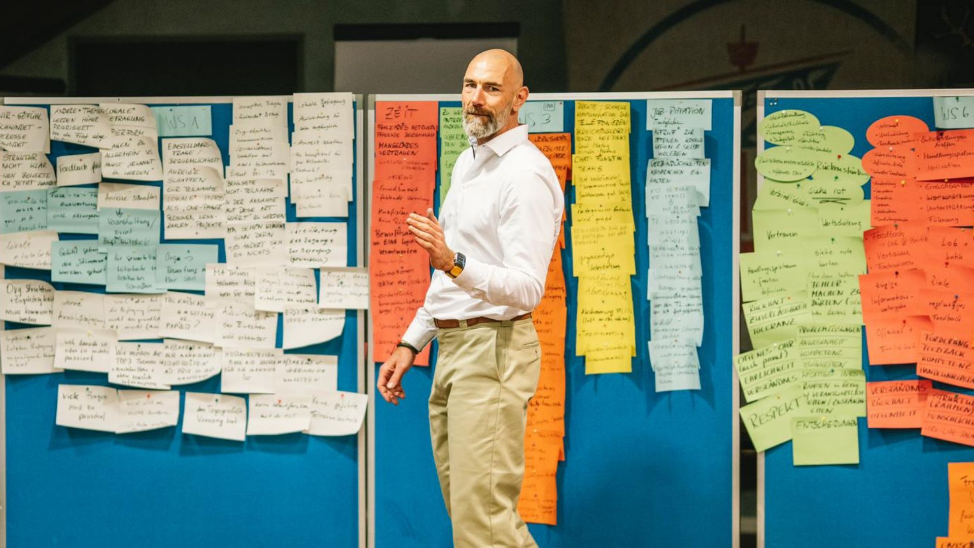 Workshop-Leiter in weißem Hemd steht vor bunter Pinnwand voller Notizen