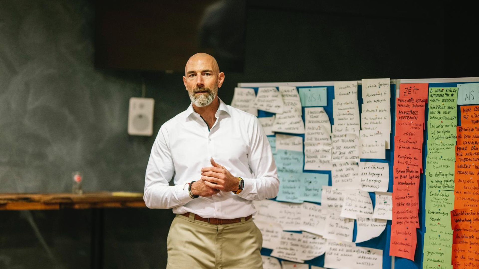 Mann steht vor Pinnwand mit bunten Notizzetteln und spricht während eines Workshops.