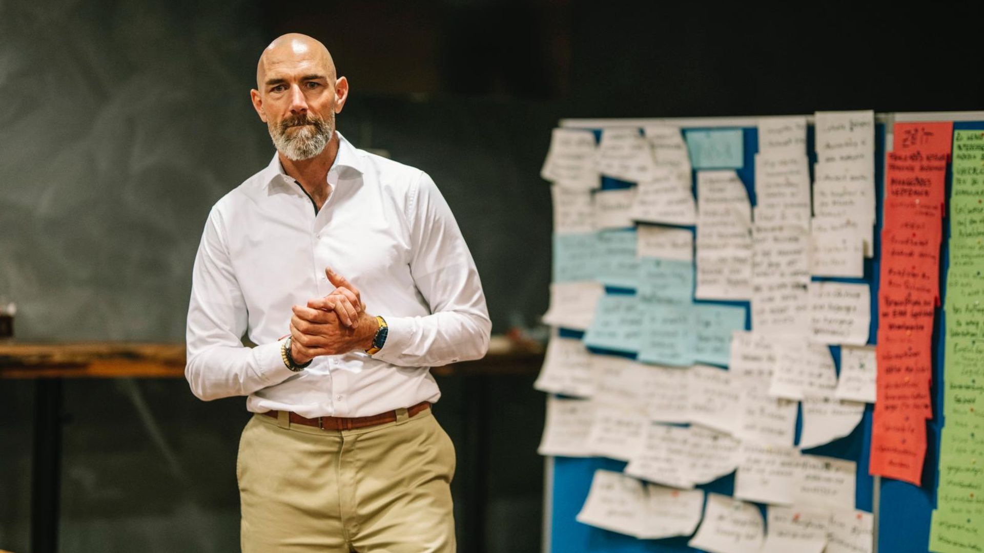 Mann in weißem Hemd steht nachdenklich vor einer Pinnwand voller Notizzettel