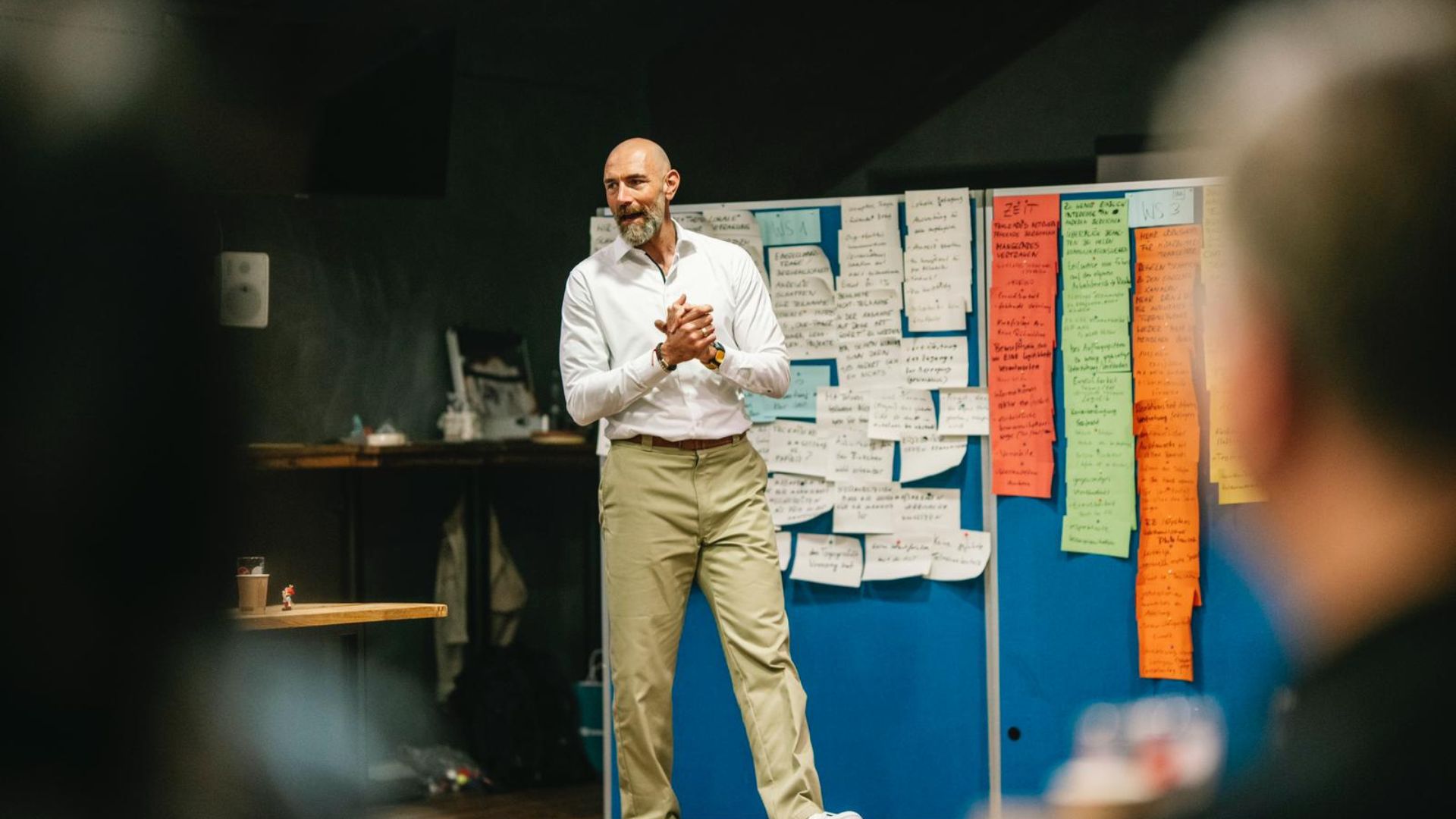 Vertriebstrainer steht vor einer voll bestückten Moderationswand und führt seine Gruppe durch den Workshop