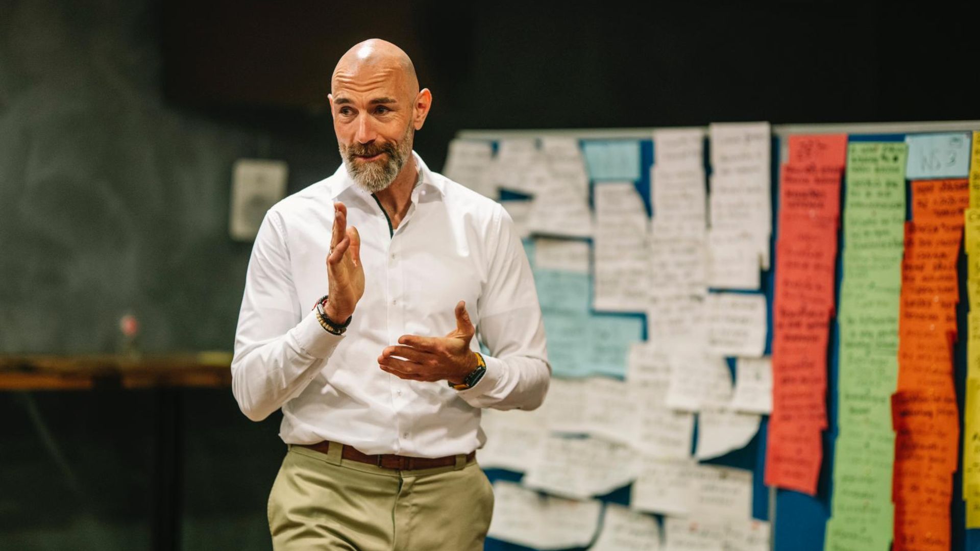 Vertriebstrainer erläutert ein Thema und gestikuliert vor einer mit Notizzetteln und farbigen Karten gefüllten Workshop-Wand.