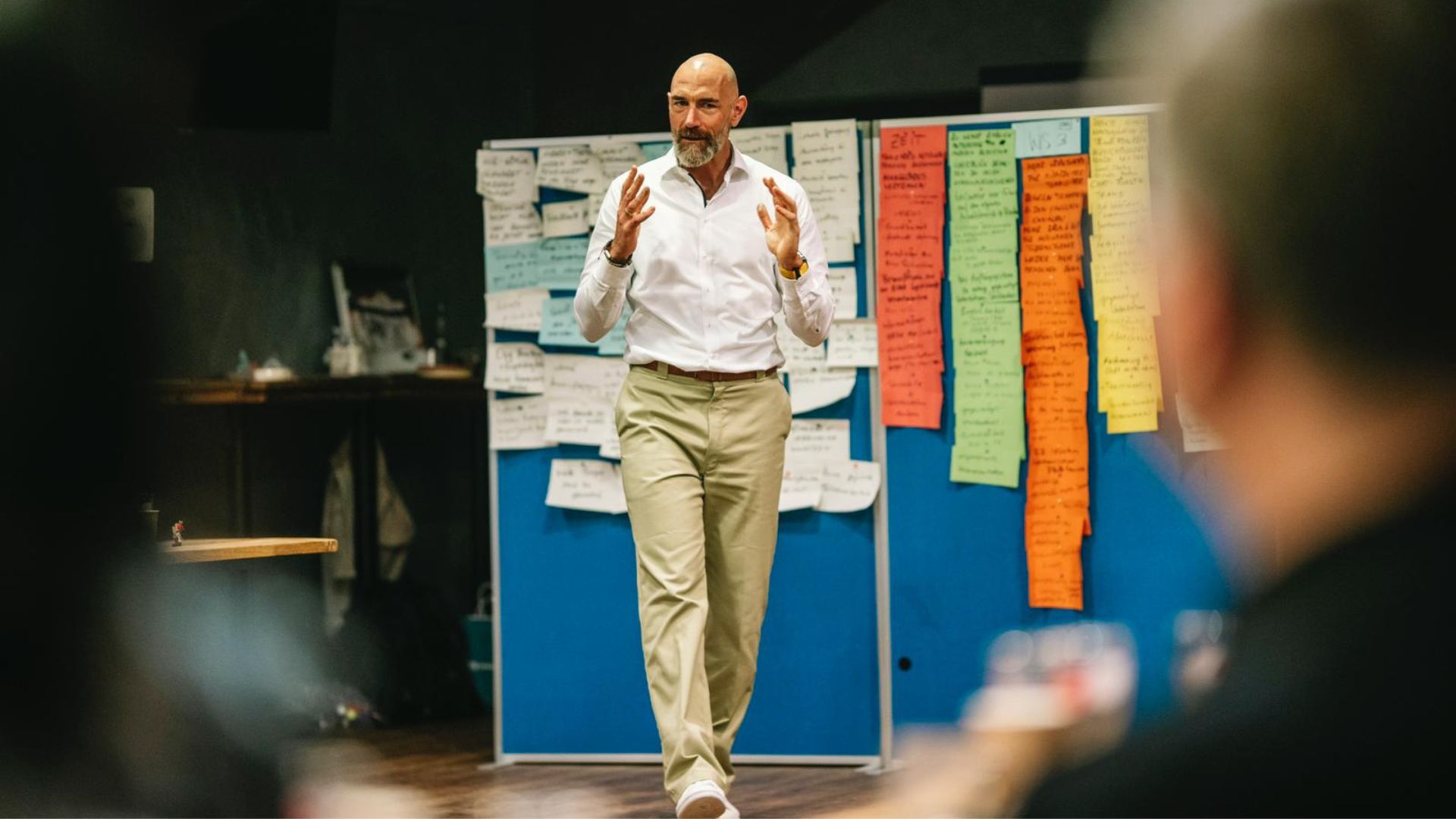 Mann spricht gestikulierend vor Pinnwand mit bunten Notizzetteln während eines Vertriebsworkshops.