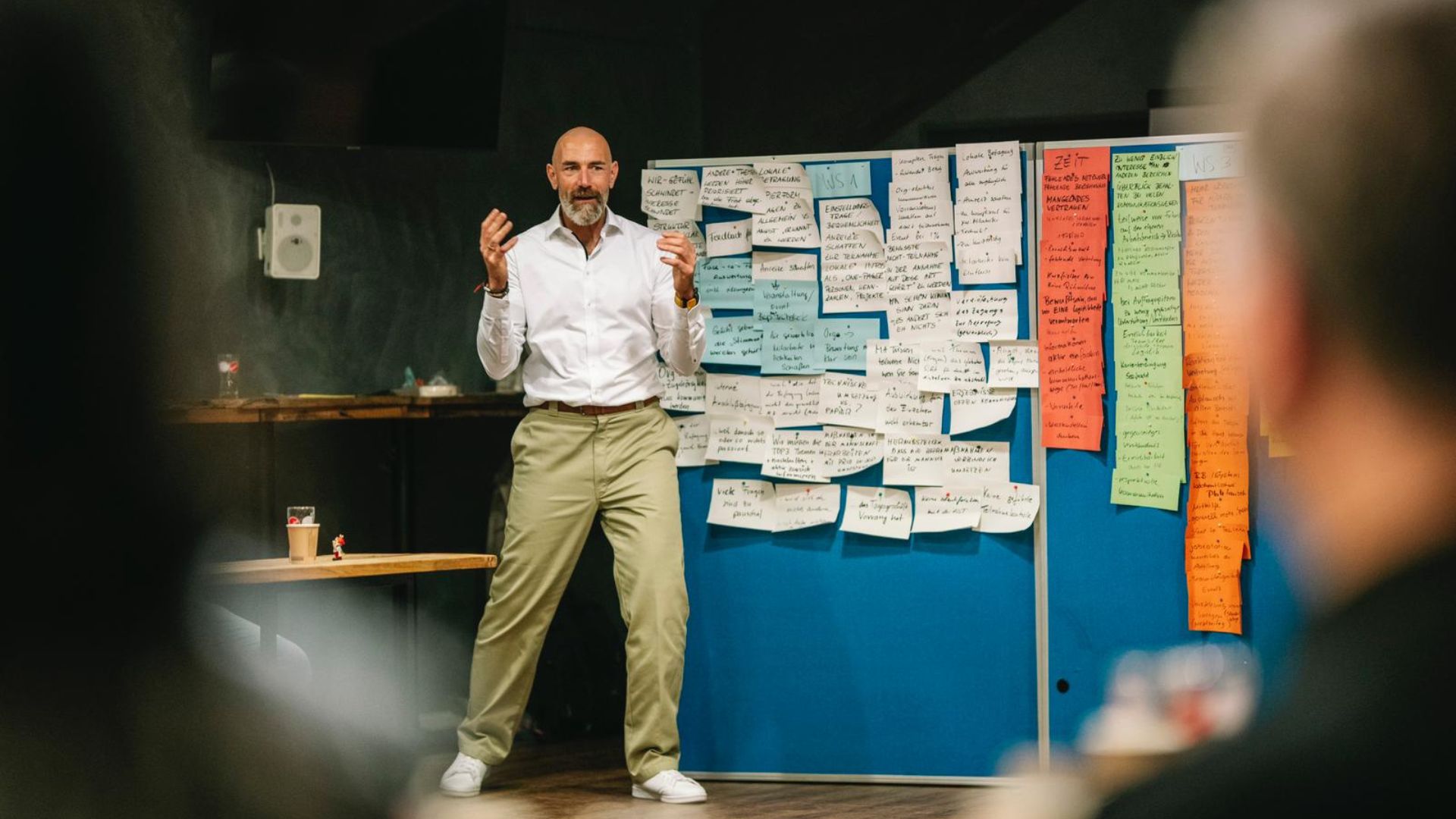 Mann in weißem Hemd präsentiert vor Pinnwand mit Notizzetteln während eines Workshops zum Thema Vertrieb.