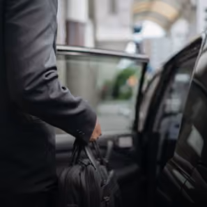 Homme en costume sombre tenant un sac en cuir noir montant dans une voiture noire