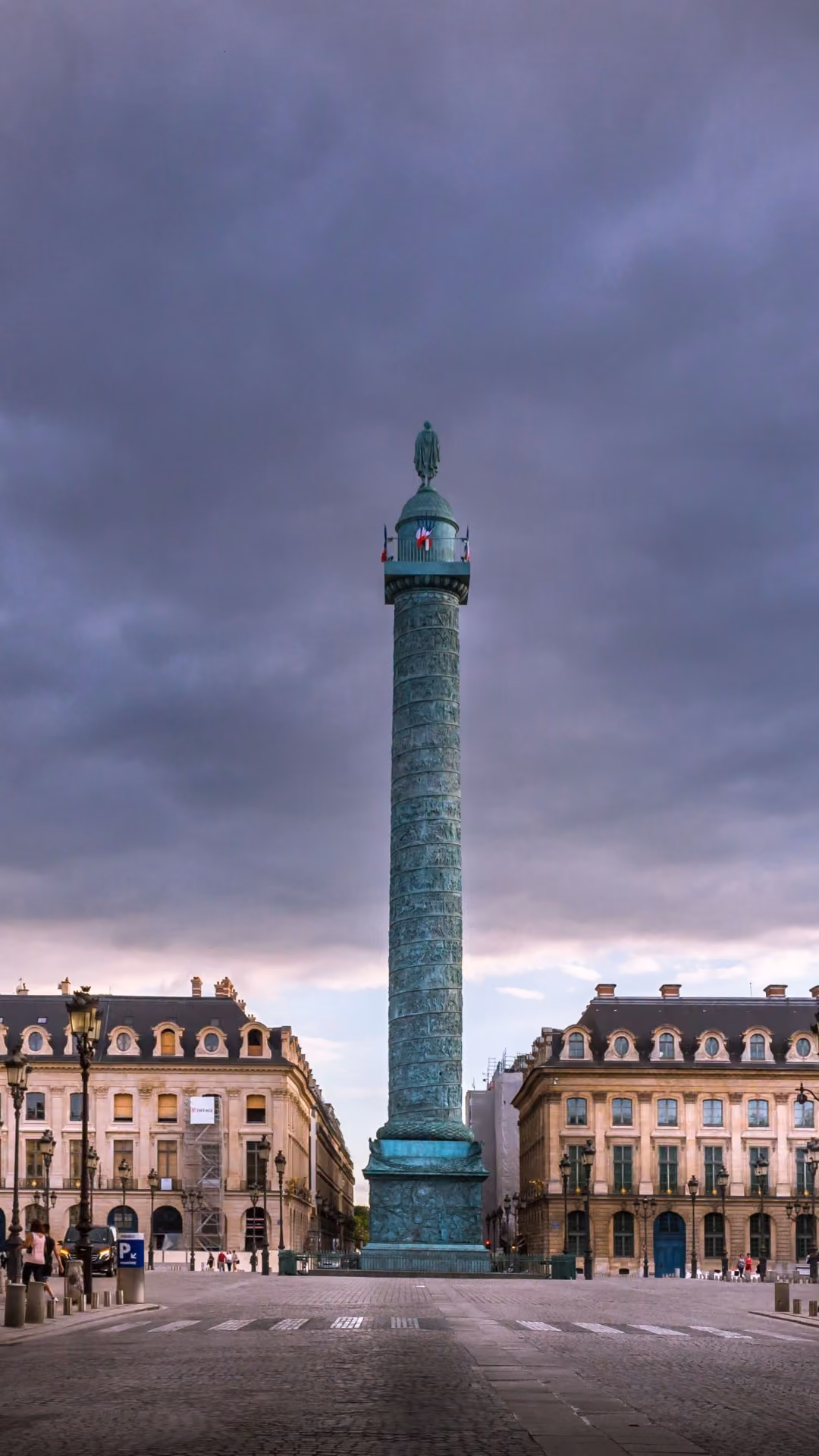 Place Vendôme avec colonne en bronze, lampadaires dorés, bâtiments haussmanniens et ciel nuageux crépusculaire