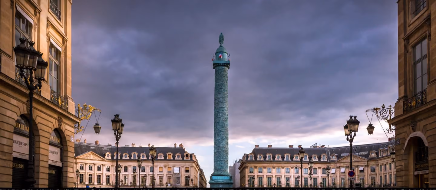 Place Vendôme avec colonne en bronze, lampadaires dorés, bâtiments haussmanniens et ciel nuageux crépusculaire