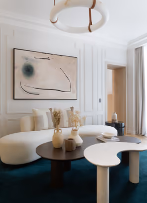 Canapé courbe blanc, tableau abstrait beige, table basse ronde sombre, tapis bleu nuit