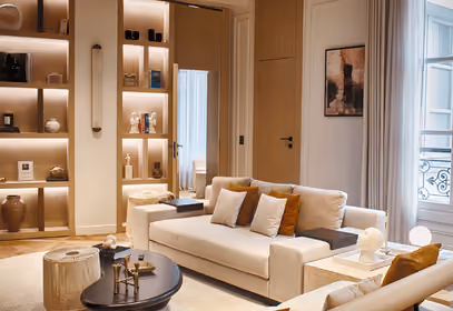 Modern elegant living room with a beige sofa and illuminated wooden bookshelves.