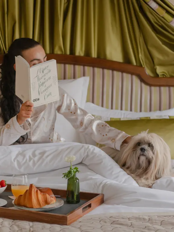 Photo of a woman reading a book in her bed accompanied by her little dog in the Hôtel Napoléon Paris - Hotel pet friendly