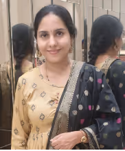 Woman with dark hair wearing a cream and black traditional outfit, standing in front of mirrored panels reflecting her image.