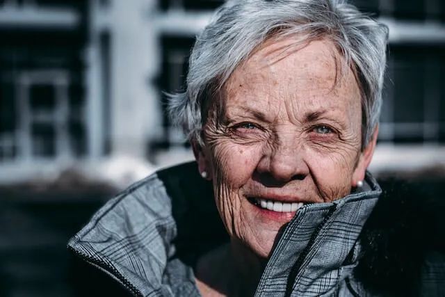 An older woman smiles warmly at the camera, showcasing her joyful expression and friendly demeanor.