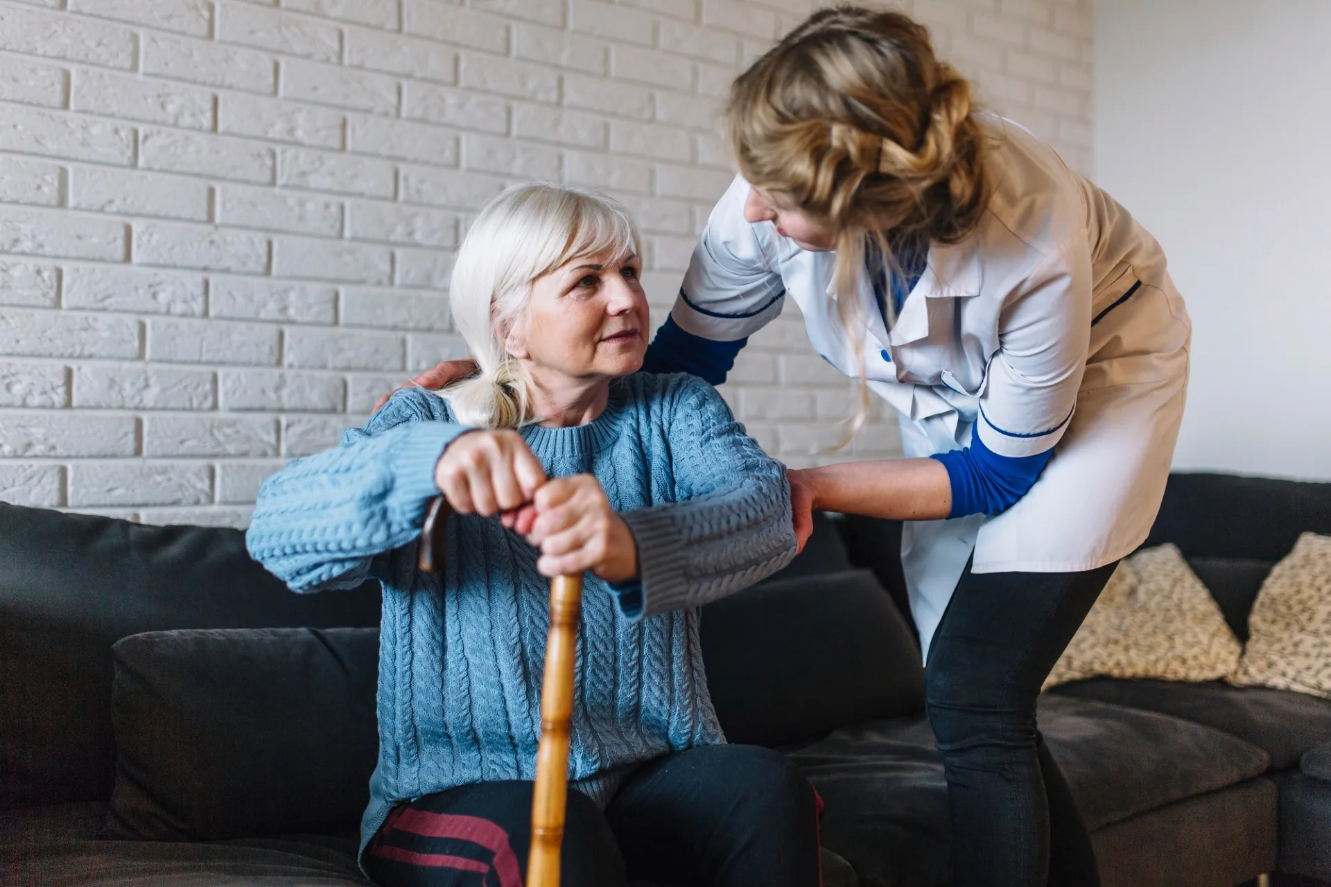 A woman assists an older woman using a cane, providing support and guidance as they walk together.