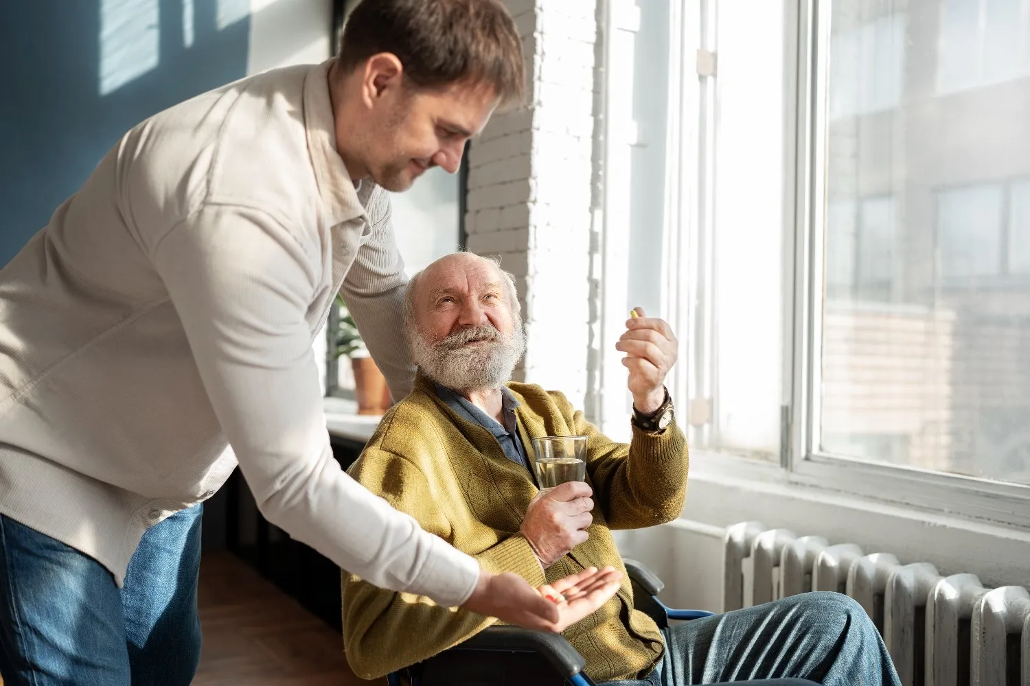 A man in a wheelchair raises a glass of wine to toast with an older man, both smiling in a warm, friendly setting.