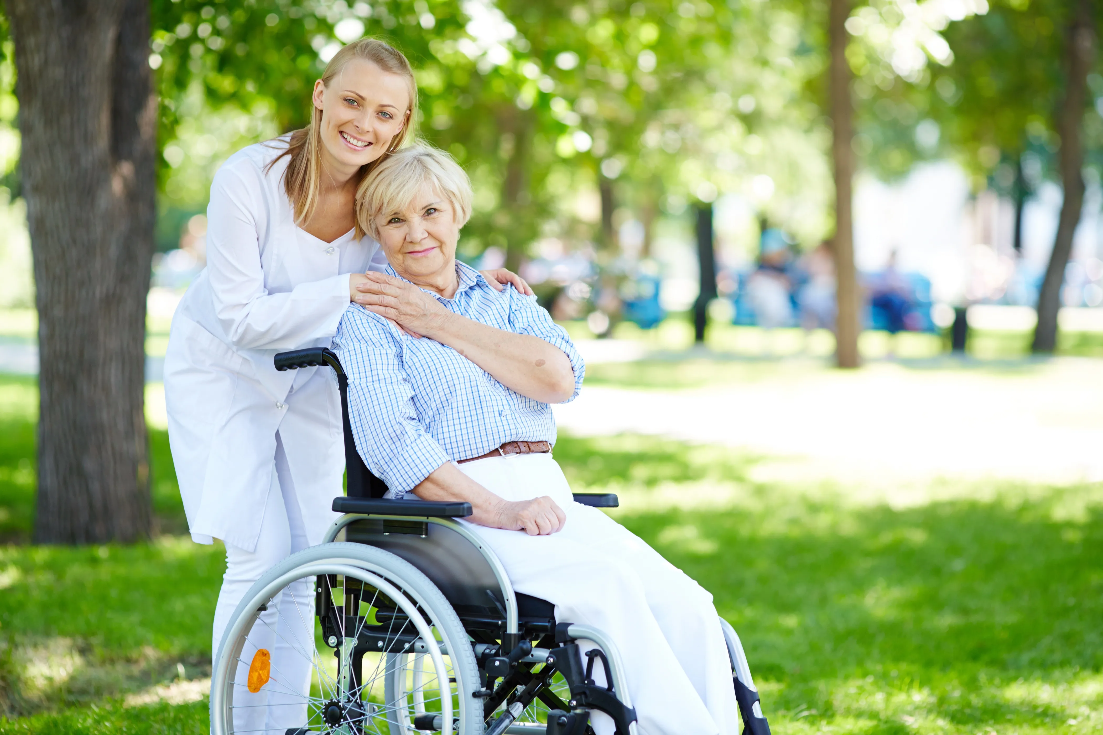 A woman in a wheelchair smiles alongside an older woman, both engaged in a warm conversation outdoors.