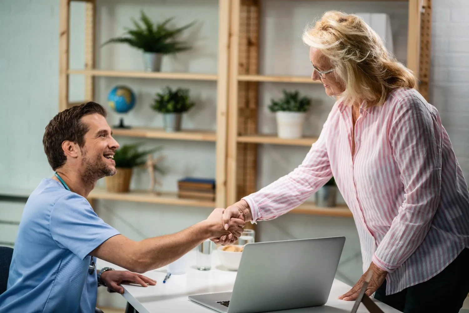 A man and woman shaking hands at a desk, symbolizing agreement or partnership in a professional setting.