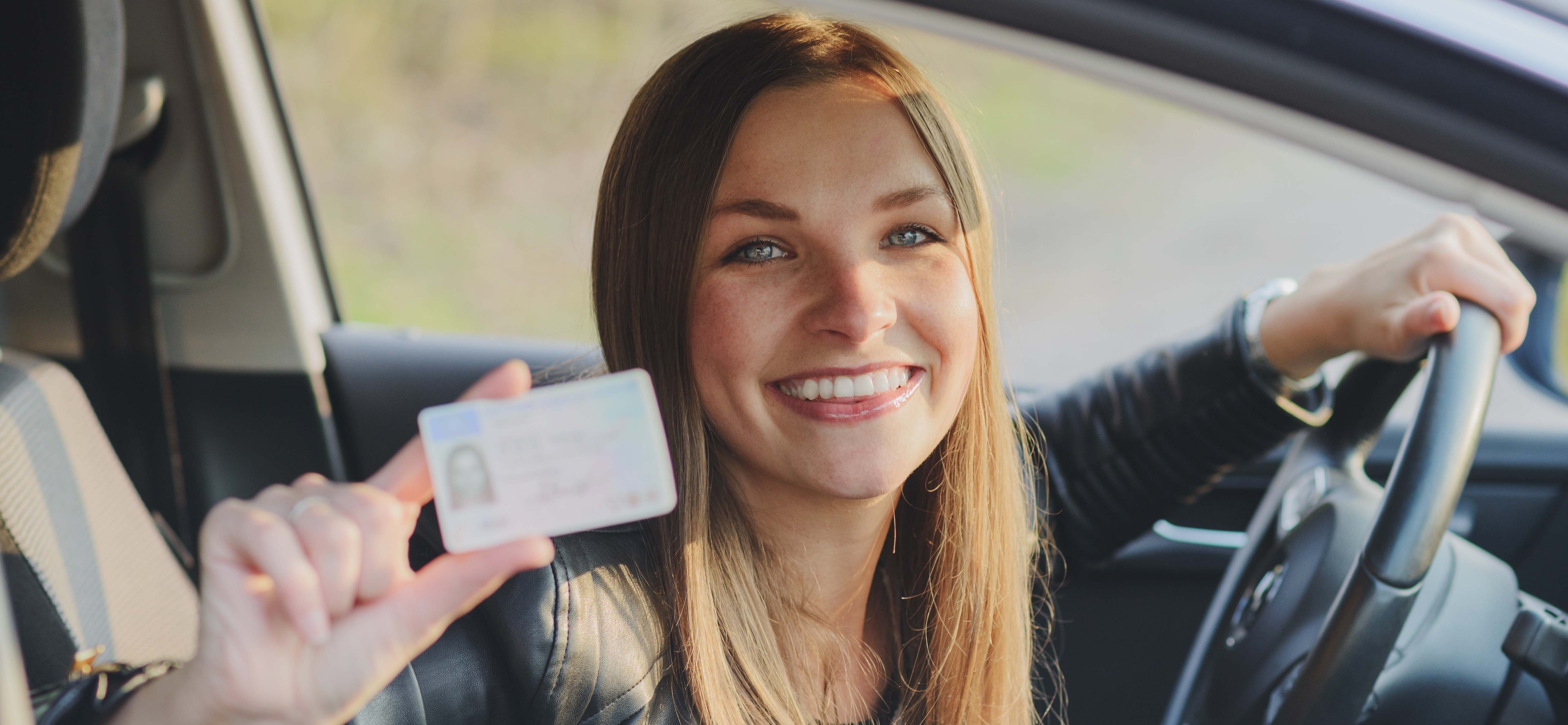 Une photo d'une jeune femme au volant montrant son permis de conduire en souriant