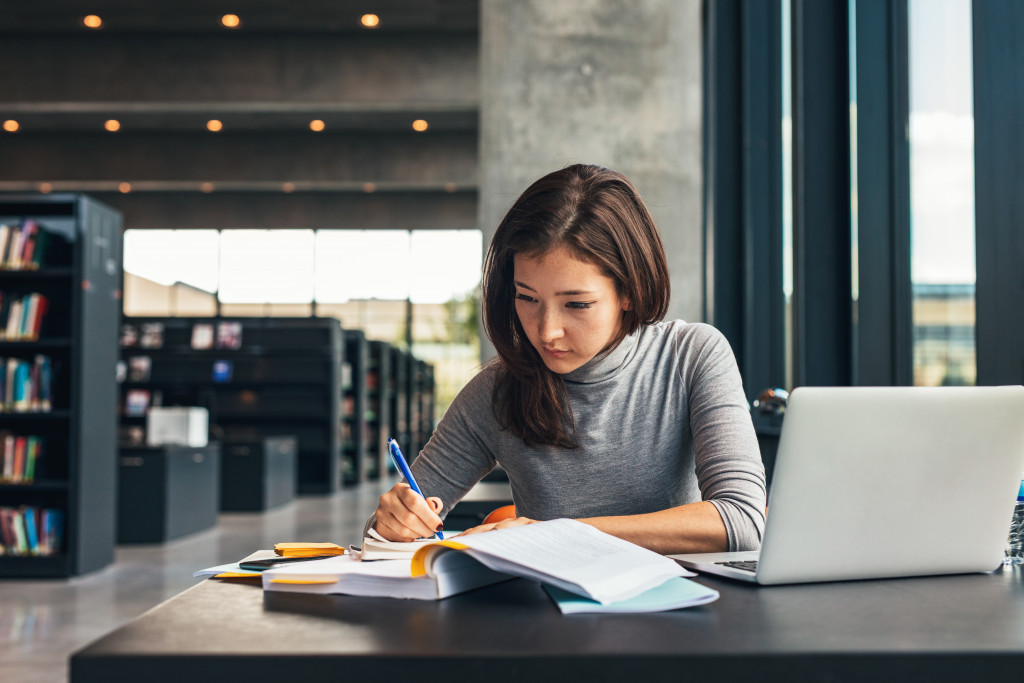 woman in a library with a laptop - How to Revise for Biology GCSE